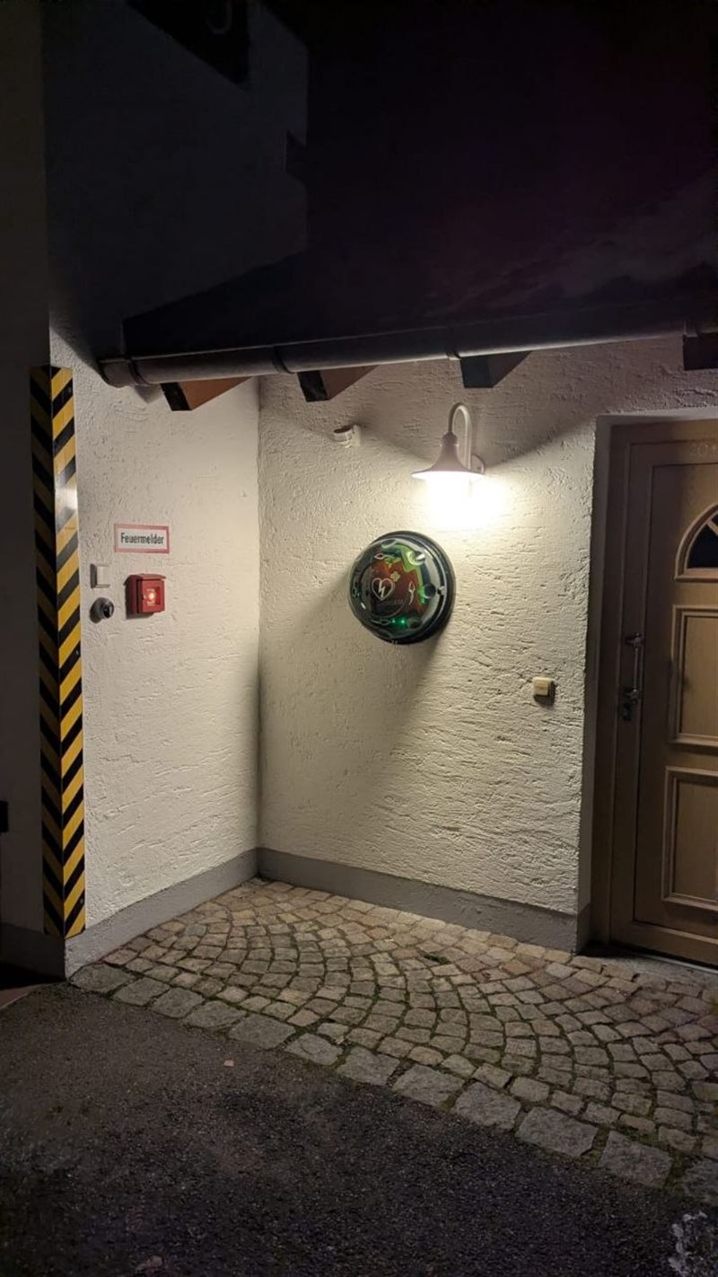 Defibrillator in einem beleuchteten Wandkasten neben der Eingangstür des Feuerwehrhauses